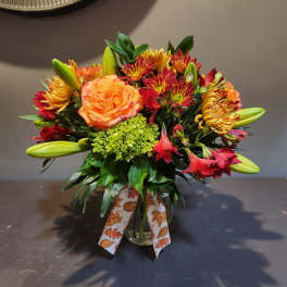 Mixed bouquet of orange roses, lilies, and red chrysanthemums in a glass vase