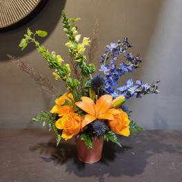 Orange lilies and roses in a brown vase with blue flowers