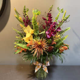 Tall mixed bouquet in a glass vase with yellow, orange, and magenta flowers