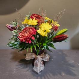 Bouquet of red and yellow flowers in a dark vase with a sheer bow