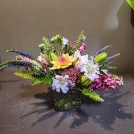 Mixed bouquet in a square glass vase with lilies, dahlias, and purple spikes