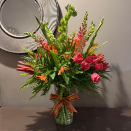 Mixed bouquet of pink and orange flowers in a glass vase with a plaid ribbon