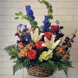 Basket arrangement with red roses, white lilies, and blue delphinium