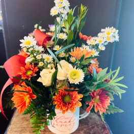 Mixed bouquet in a white mug with orange and white flowers and red ribbon