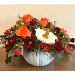 Orange roses and red flowers arranged in a white pumpkin vase