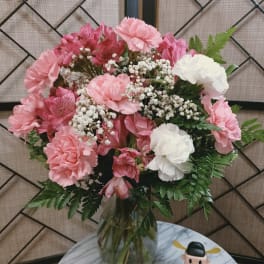 Pink and white bouquet in a glass vase with a small figurine beside it