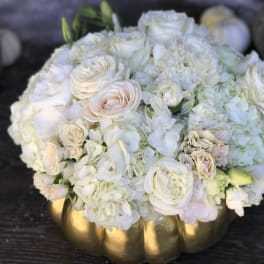 White roses and hydrangeas arranged in a gold pumpkin vase