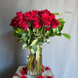 Red roses in a clear glass vase with scattered petals