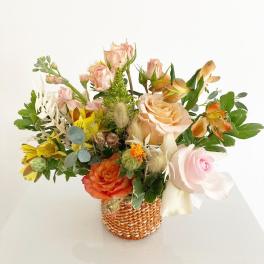 Mixed bouquet in a woven basket with peach, pink, and yellow flowers