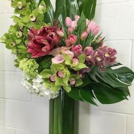 Tall floral arrangement with orchids, tulips, and lilies in a glass vase