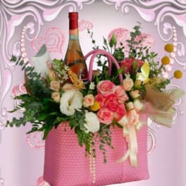Pink gift basket with roses, white flowers, and a wine bottle