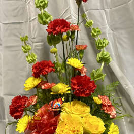 Yellow and red floral arrangement in a round container with a red ribbon