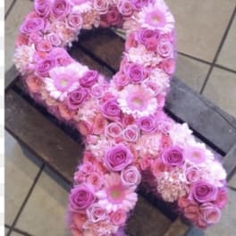Pink floral arrangement shaped like an awareness ribbon on a wooden crate
