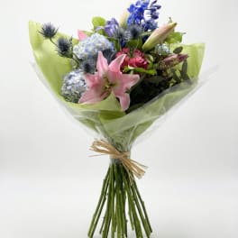 Bouquet of pink lilies, blue hydrangeas, and purple flowers wrapped in green paper