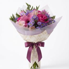 Pink and purple mixed bouquet wrapped in patterned paper with a satin ribbon