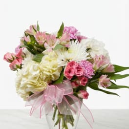 Pink and white mixed bouquet in a clear glass vase with a pink ribbon