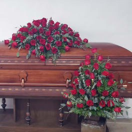 Red rose casket spray and standing floral arrangement on a wooden casket