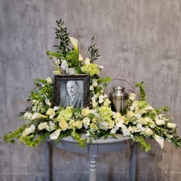 Sympathy floral tribute with a framed portrait and urn surrounded by white flowers
