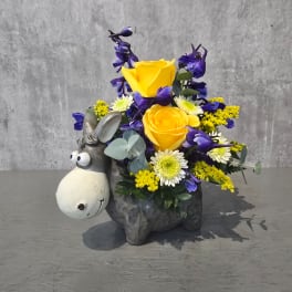 Yellow roses and purple flowers arranged in a donkey figurine container