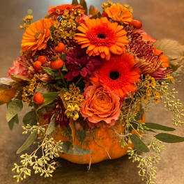 Orange and burgundy floral arrangement in a pumpkin container