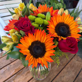 Bouquet of orange sunflowers and red roses in a glass vase