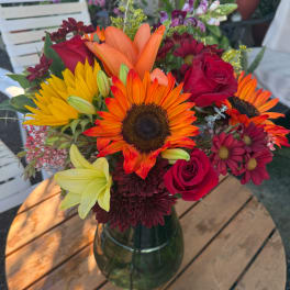 Mixed bouquet with sunflowers, red roses, lilies, and chrysanthemums in a glass vase