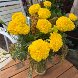 Yellow marigold bouquet in a clear glass vase on a wooden table