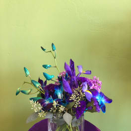 Purple and blue floral arrangement in a clear square vase