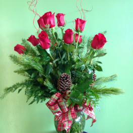 Red roses arranged in a glass vase with pinecones and plaid ribbon