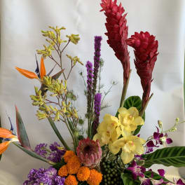 Tropical floral arrangement with red ginger, yellow orchids, and purple blooms in a black container