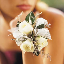 White floral wrist corsage with roses and ribbon on a person's wrist