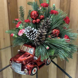 Holiday arrangement in a red toy truck with pine, pinecones, and red accents