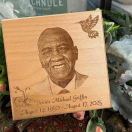 Wooden memorial plaque with a portrait and engraved dates, surrounded by flowers