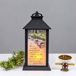 Black lantern with a memorial message and a small greenery sprig beside it