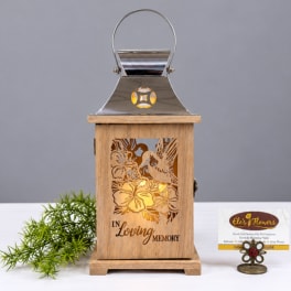 Wooden memorial lantern with metal top and floral cutouts, lit from within