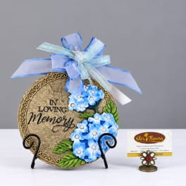Decorative memorial plaque with blue flowers and ribbon on a stand
