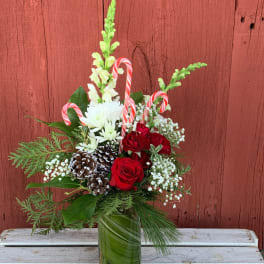 Christmas bouquet with red roses, white blooms, and candy canes in a glass vase