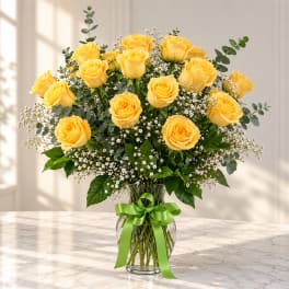 Yellow roses in a glass vase with a green ribbon
