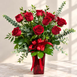 Red roses arranged in a red glass vase with a ribbon bow