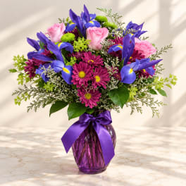 Bouquet of pink roses, purple irises, and magenta daisies in a purple vase