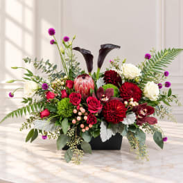 Mixed floral arrangement in a black rectangular vase with red, white, and purple blooms
