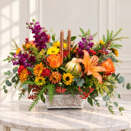 Autumn floral centerpiece with orange lilies, roses, and candles in a square vase