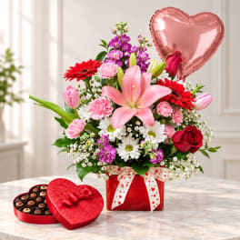 Mixed bouquet in a red box with a heart balloon and chocolate box beside it.