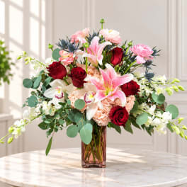 Mixed bouquet of pink lilies, red roses, and white orchids in a glass vase