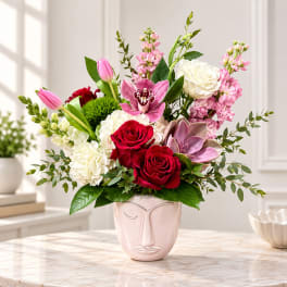 Mixed bouquet of roses, tulips, orchids, and hydrangeas in a pink face vase
