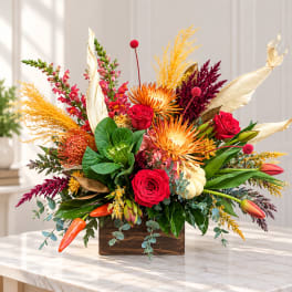 Bright mixed floral arrangement in a wooden box with red roses and orange blooms