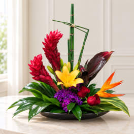 Tropical flower arrangement with red ginger, yellow lily, and bamboo in a low black dish