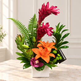 Tropical flower arrangement with orange lilies and pink orchids in a white vase