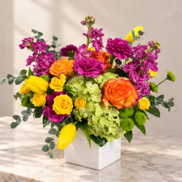 Colorful bouquet in a white square vase with roses, tulips, hydrangea, and purple blooms