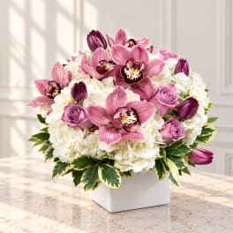 Pink orchids and roses arranged in a white square vase